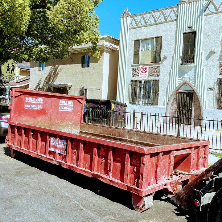Red roll-off dumpster loaded with renovation debris outside a Los Angeles apartment building