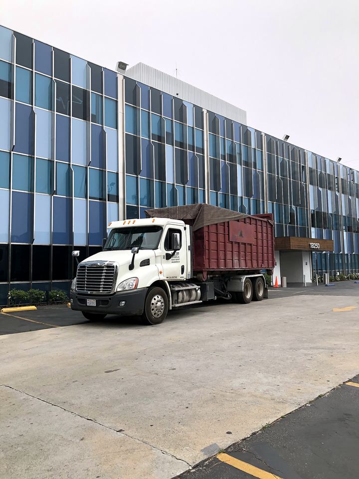 Roll-off dumpster truck servicing a commercial office building in Los Angeles