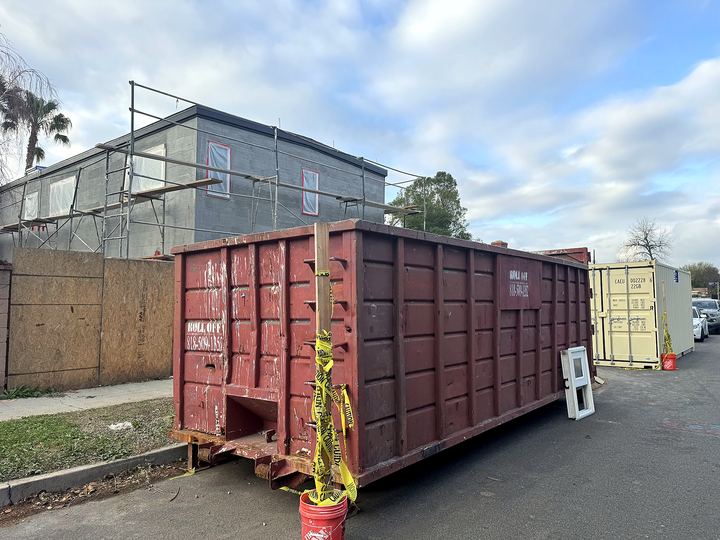 Roll-off construction dumpster next to scaffolding on a Los Angeles remodel