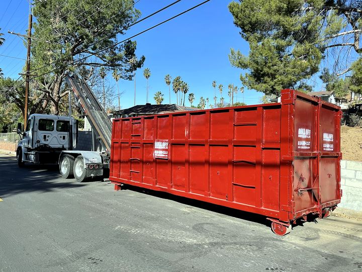 Roll-off dumpster being lowered into place on a narrow tree-lined residential street