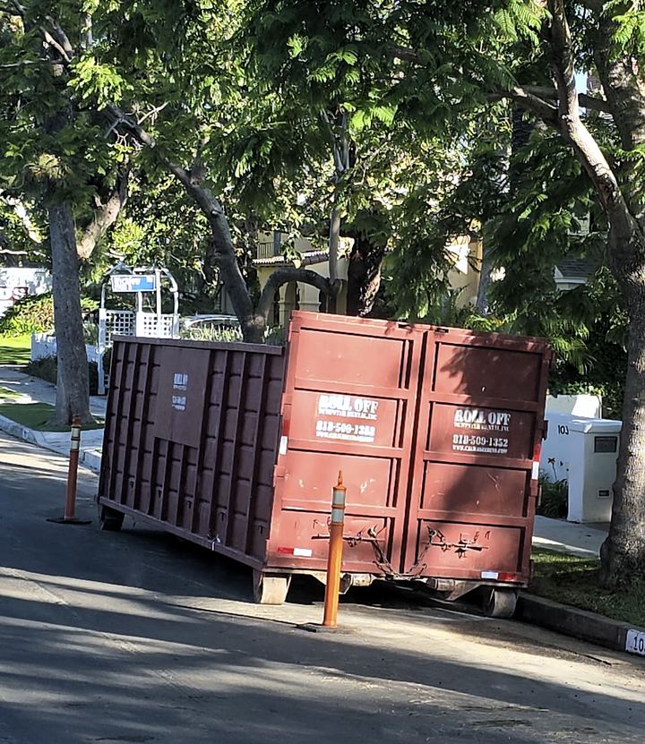 Roll-off dumpster placed beside staged construction materials on a Los Angeles job site