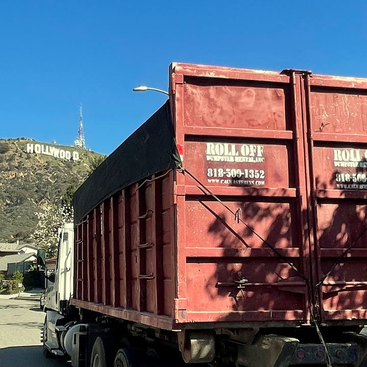 Red roll-off dumpster on a job with the Hollywood sign visible in the background