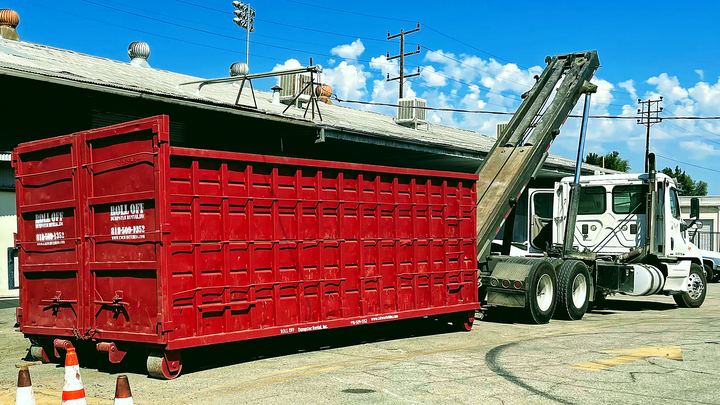 Red roll-off dumpster hooked to a Roll Off Dumpster Rental truck ready for haul